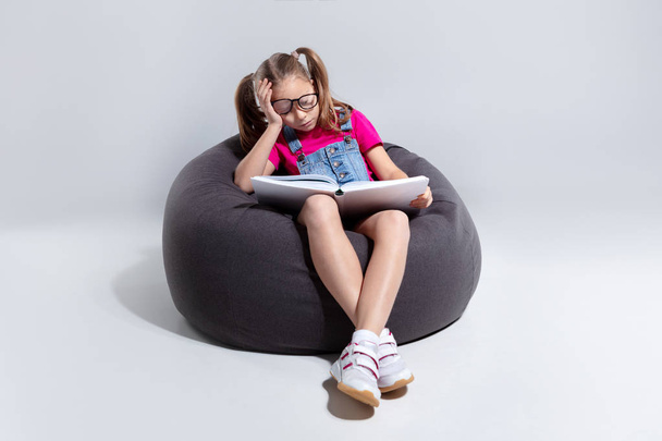 Giovane ragazza in occhiali dormire con un libro su un sacchetto di fagioli grigi
 - Foto, immagini