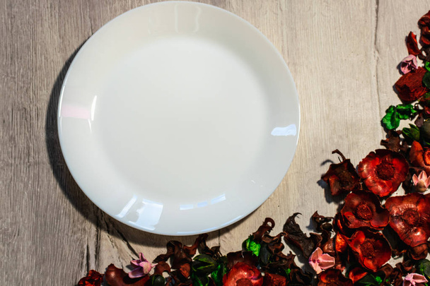 Empty white plate on a wooden background decorated with dry flower petals. View from above. - Valokuva, kuva