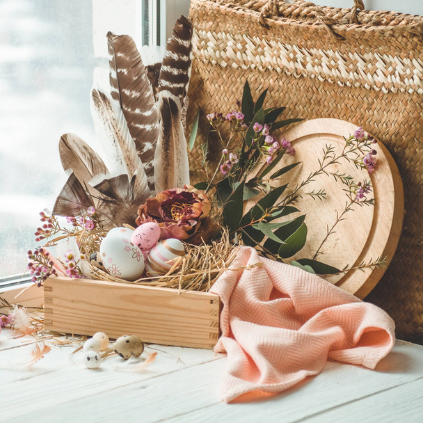 Ευτυχισμένο Πάσχα φόντο. Ροζ Πασχαλινά αυγά σε φωλιά με floral διακοσμήσεις και τα φτερά κοντά στο παράθυρο. Ορτύκια αυγά. Ευτυχισμένο Πάσχα έννοια. - Φωτογραφία, εικόνα