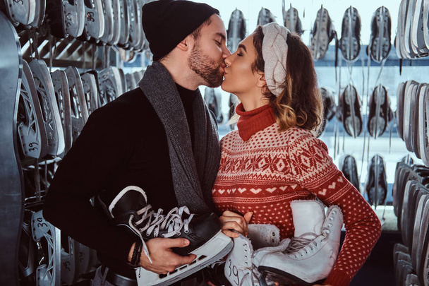 Giovane coppia innamorata, bacio mentre in piedi vicino rack con molte coppie di pattini
 - Foto, immagini
