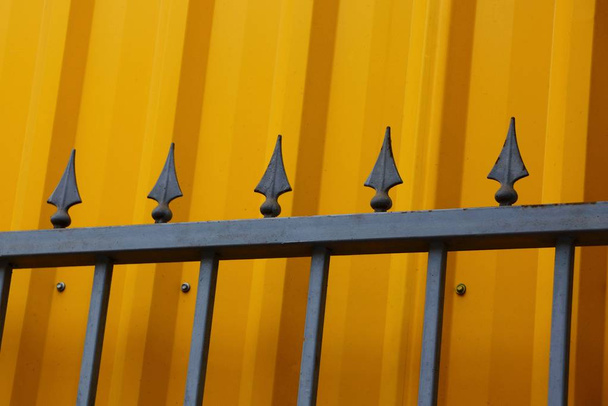 Teil des eisernen Zauns aus schwarzen, scharfen Stangen vor dem Hintergrund der gelben Mauer - Foto, Bild