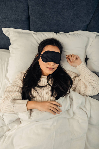Asian woman wearing black sleeping mask lying in bed - Fotografie, Obrázek