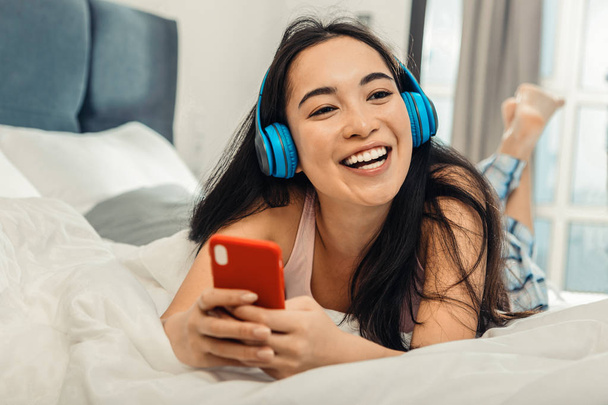 Beautiful woman wearing pajama lying on bed and listening to music - Fotoğraf, Görsel