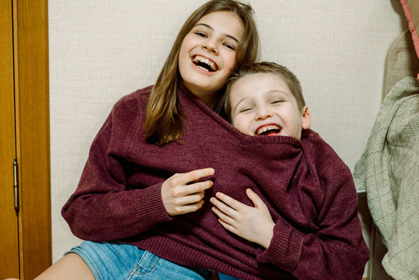the kids are joking, one sweater for two, laughing and dabbling. Brother and sister are funny. Fool's day concept - Zdjęcie, obraz