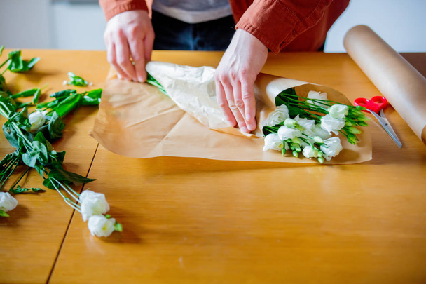 Cropped view of man wrapping white roses on kitchen table. Own business concept. - Photo, Image