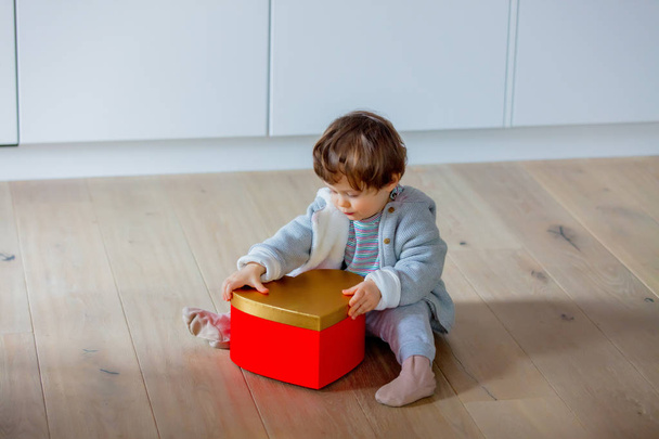 Маленький маленький хлопчик сидить на підлозі з червоною і золотистою коробкою для серця Валентина
.   - Фото, зображення