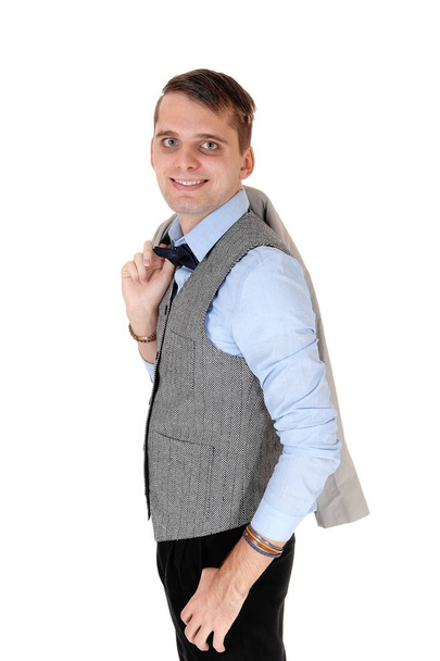 Een knappe jongeman die permanent in een grijze vest en donkere broek met hi - Foto, afbeelding
