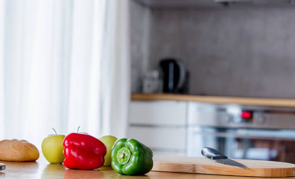grüne und rote Paprika mit Apfel und Messer auf einem Holztisch.  - Foto, Bild