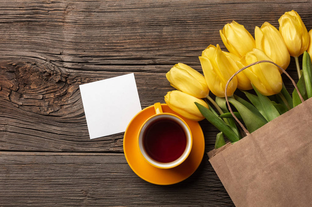 Желтые тюльпаны, чашка чая и пасхальные яйца на деревянном фоне. Вид сверху с пространством для копирования
 - Фото, изображение