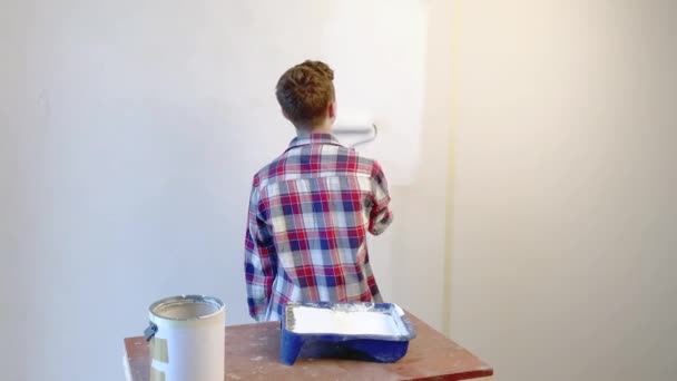 Tini fiú festés belső falak segítségével FESTŐHENGER lakás hátulnézete. Csinos kamasz maga teszi javítások szobájába - festékek fal. Otthon felújítása vagy Redecoration koncepció. - Felvétel, videó