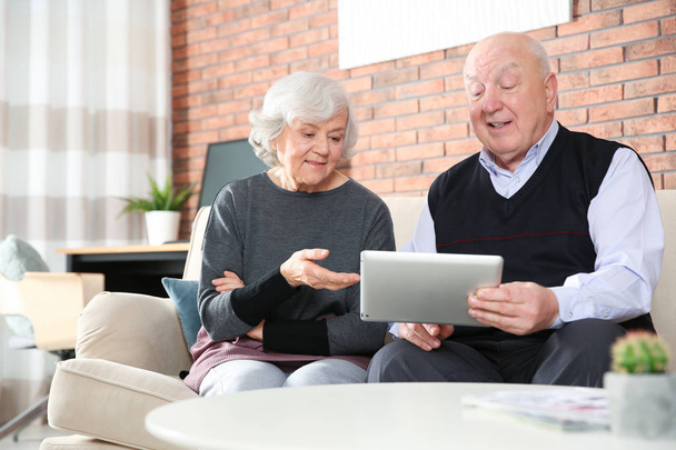 Elderly couple using tablet PC on sofa in living room - Φωτογραφία, εικόνα