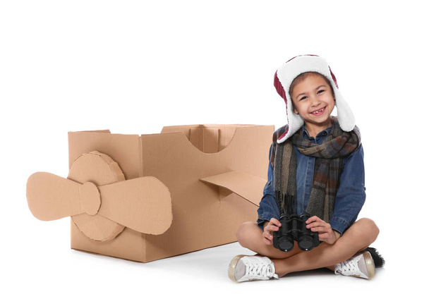 Cute little girl playing with binoculars and cardboard airplane on white background - Foto, afbeelding