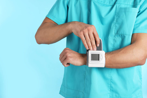 Male doctor using blood pressure monitor on color background, closeup. Medical object - Foto, imagen