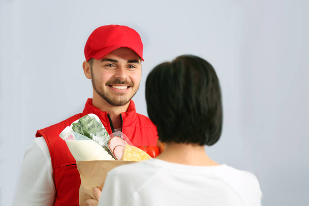 Male courier delivering food to client on light background - Fotó, kép