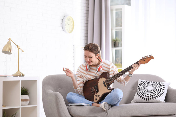 Young woman with electric guitar composing song in living room - Foto, afbeelding
