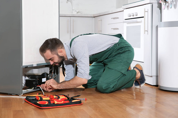 Male technician in uniform repairing refrigerator indoors - Foto, Imagem