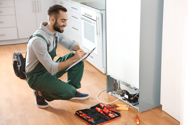 Techniker mit Klemmbrett untersucht Kühlschrank in Küche - Foto, Bild