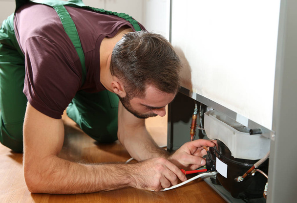 Técnico masculino en uniforme reparando refrigerador en interiores
 - Foto, Imagen