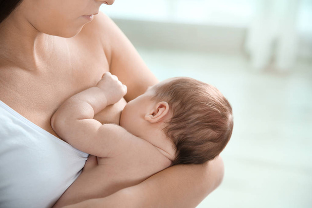 Jonge vrouw borstvoeding haar baby op onscherpe achtergrond, close-up - Foto, afbeelding