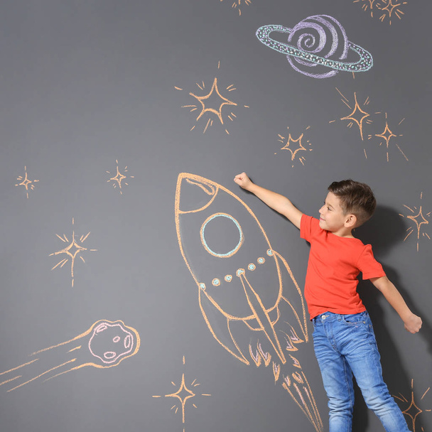 Cute little child playing with chalk rocket drawing on grey background - Photo, image