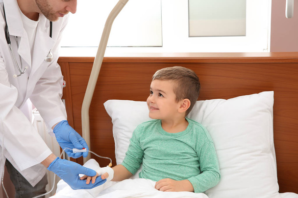 Médico ajustando gotejamento intravenoso para criança pequena no hospital
 - Foto, Imagem
