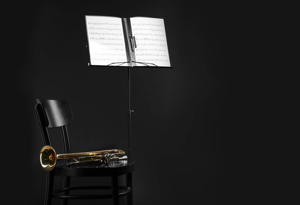 Trumpet, chair and note stand with music sheets on black background. Space for text - Фото, зображення
