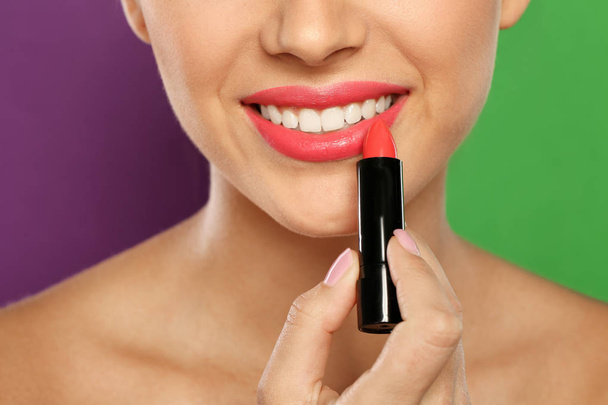 Young woman applying lipstick on color background, closeup - 写真・画像
