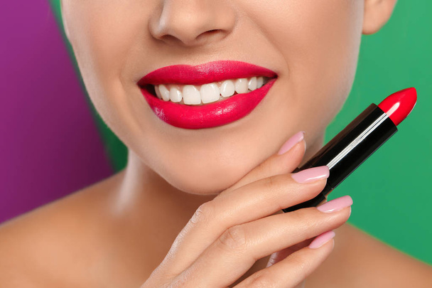 Young woman applying lipstick on color background, closeup - Valokuva, kuva