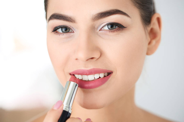 Young woman applying lipstick on blurred background - Zdjęcie, obraz