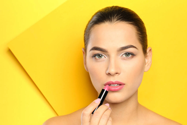 Young woman applying lipstick on color background - Foto, Imagem