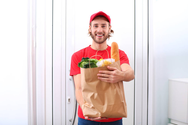 Delivery man holding paper bag with food products indoors - Foto, afbeelding
