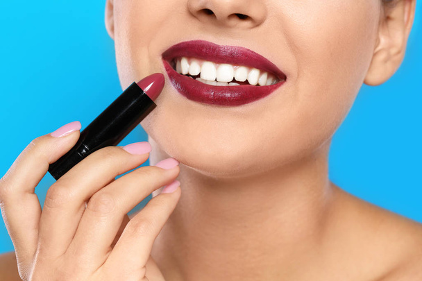 Jonge vrouw lippenstift toe te passen op kleur achtergrond, close-up - Foto, afbeelding