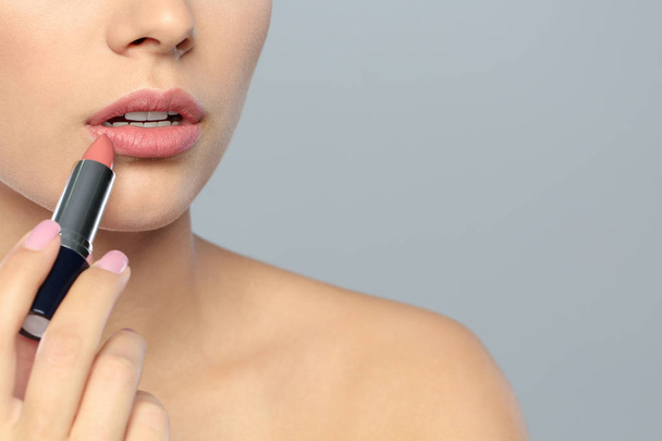 Jonge vrouw lippenstift toe te passen op kleur achtergrond, close-up. Ruimte voor tekst - Foto, afbeelding