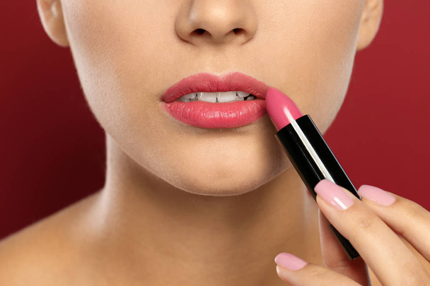 Young woman applying lipstick on color background, closeup - Фото, изображение