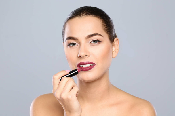 Young woman applying lipstick on color background - Foto, imagen