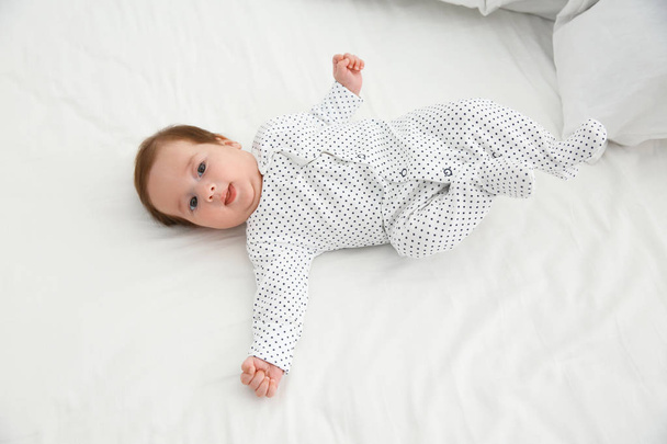 Adorable baby in cute footie on white sheet, above view - Photo, Image