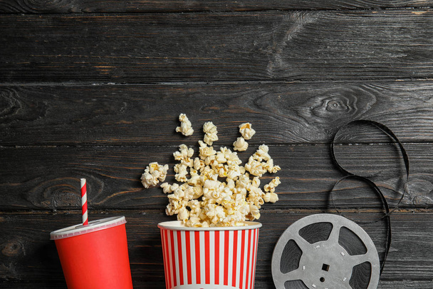 Popcorn, reel and drink on wooden background, space for text. Cinema snack - Φωτογραφία, εικόνα