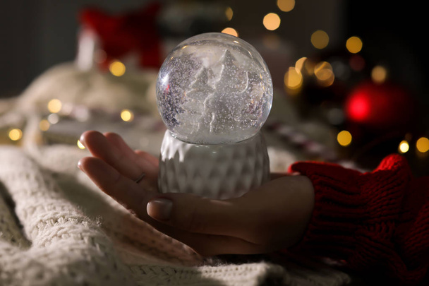 Woman holding Christmas snow globe on blurred background, closeup - Foto, imagen