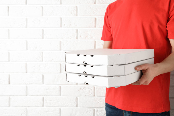 Young man with pizza boxes near white brick wall, space for text. Food delivery service - Foto, Bild