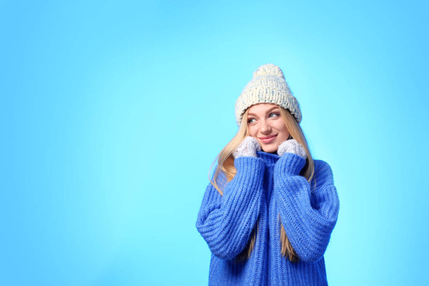 Portrait of emotional young woman in stylish hat, sweater and mittens on color background, space for text. Winter atmosphere - Zdjęcie, obraz