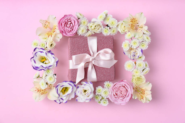 Frame of flowers and gift box on color background, top view - Foto, imagen