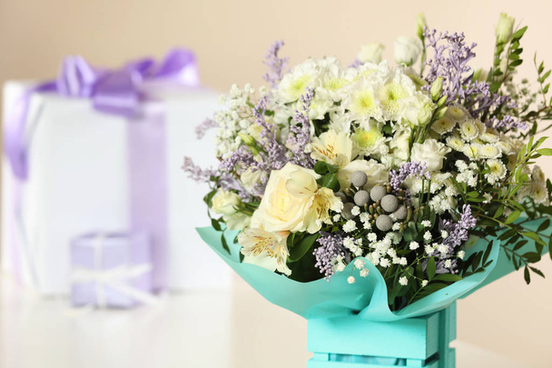 Beautiful bouquet of flowers and blurred gifts on background, closeup. Space for text - Foto, Imagem