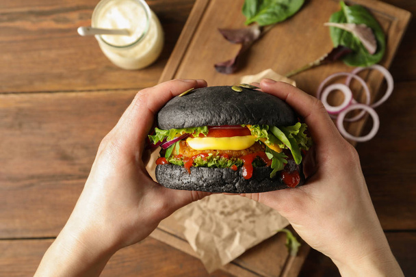 Woman holding tasty black vegetarian burger over table, top view - Foto, immagini
