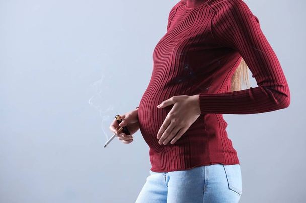 Young pregnant woman smoking cigarette on grey background, closeup. Space for text - Valokuva, kuva