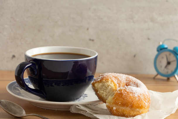 Donut recubierto de azúcar sobre papel arrugado con una taza de café, sobre una mesa de madera
. - Foto, Imagen