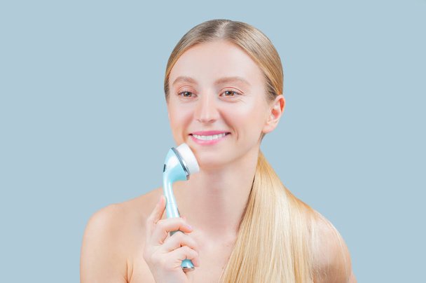 Beautiful woman is washing face skin with brush. Facial beauty treatment concept. - Zdjęcie, obraz