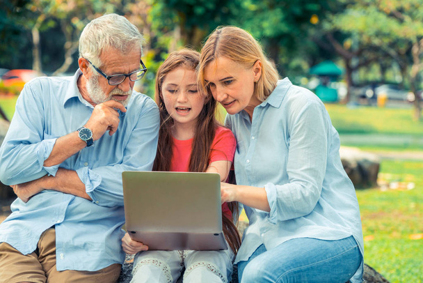 Famille heureuse utilisant ordinateur portable ensemble dans le parc de jardin en été. Concept d'éducation des enfants et d'activités familiales
. - Photo, image