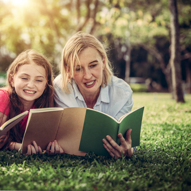Bonne famille lire des livres ensemble et couché sur l'herbe verte dans le parc public. Petite fille enfant apprenant avec mère dans le jardin extérieur. Éducation et mode de vie familial
. - Photo, image