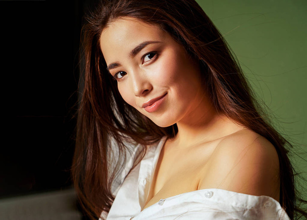 Красивый модный портрет сексуальной чувственной улыбающейся молодой женщины с темными длинными волосами в белой рубашке на зеленом фоне
 - Фото, изображение