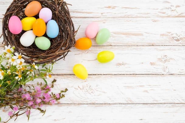 Colorful Easter eggs in nest with flower on rustic wooden planks background in white paint . Holiday in spring season. vintage color tone style. top view composition. - Fotoğraf, Görsel